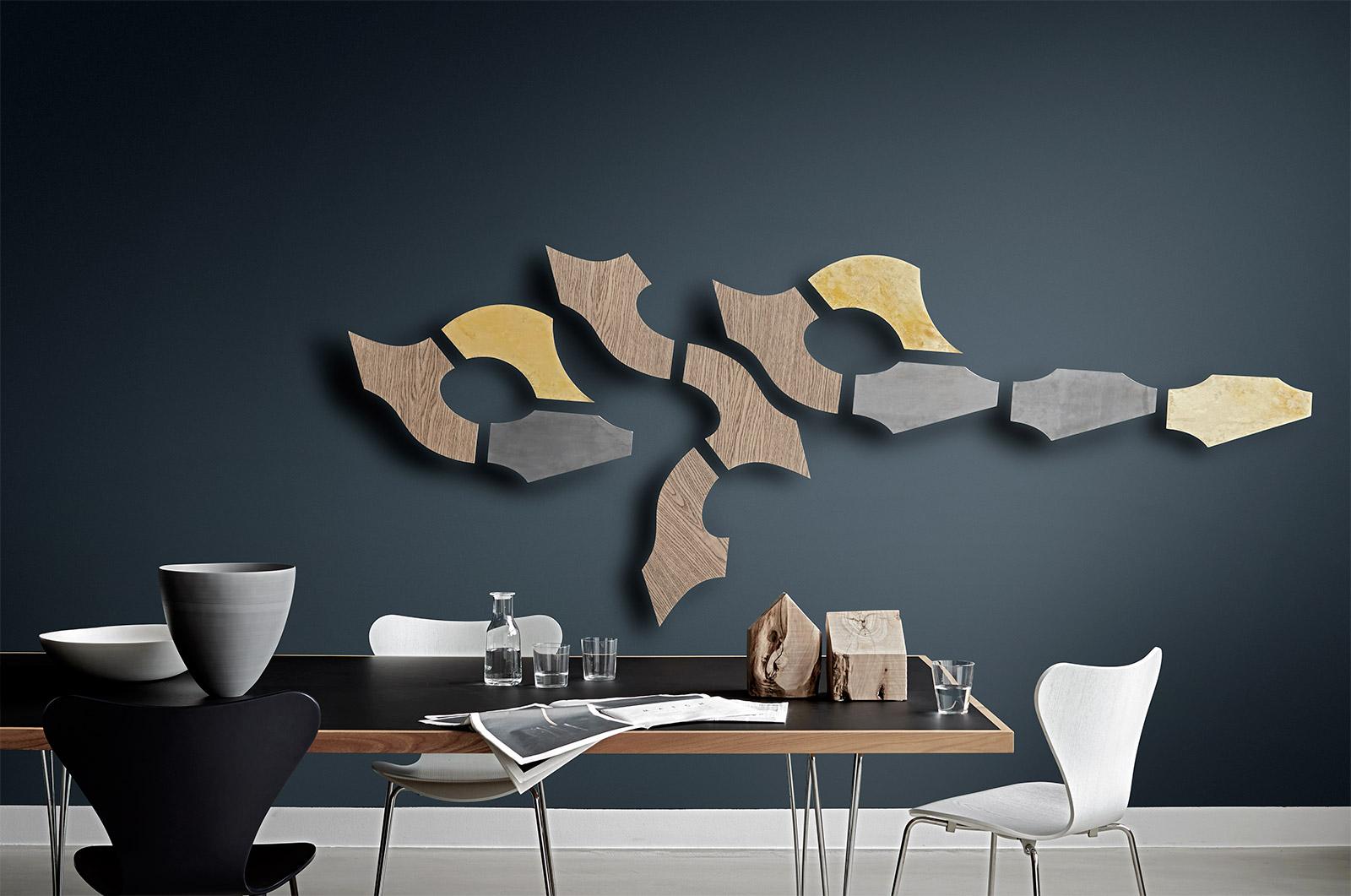 Spiseområde med mørk væg, kunst i træ og metal samt bord og stole i moderne og stilren indretning.