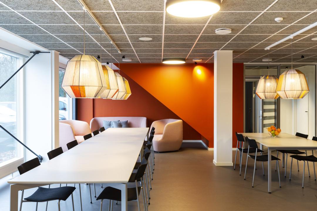 Kontor med spiseområde, lange borde, stole og pendellamper i moderne miljø.