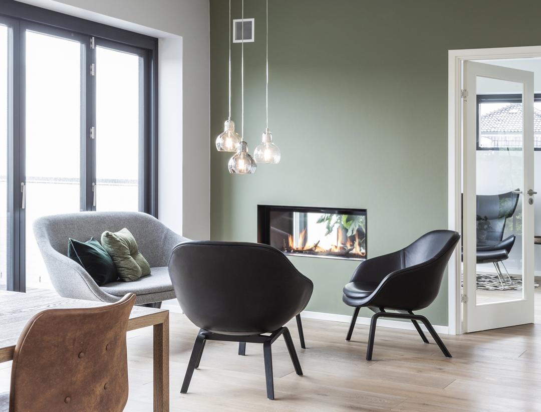 Lænestole og sofa nær en pejs indbygget i en grøn væg, elegant enkel stil