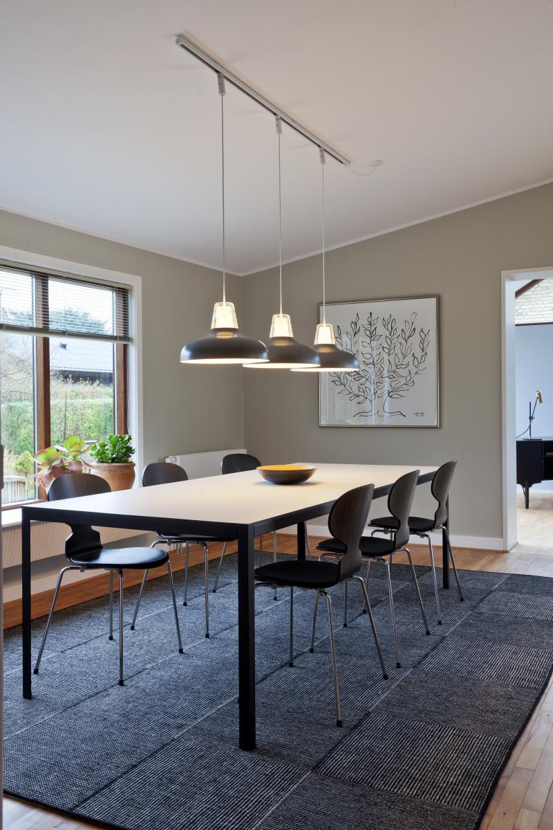 Spisestue med et stort bord og sorte stole, hængende lamper over bordet, enkel og elegant stil.
