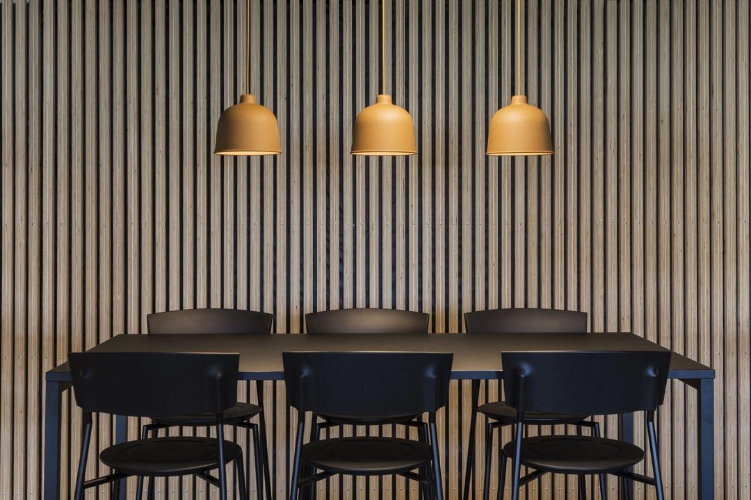 Moderne spiseplads med sorte stole, træpanelvæg og tre varme pendellamper i nordisk stil.