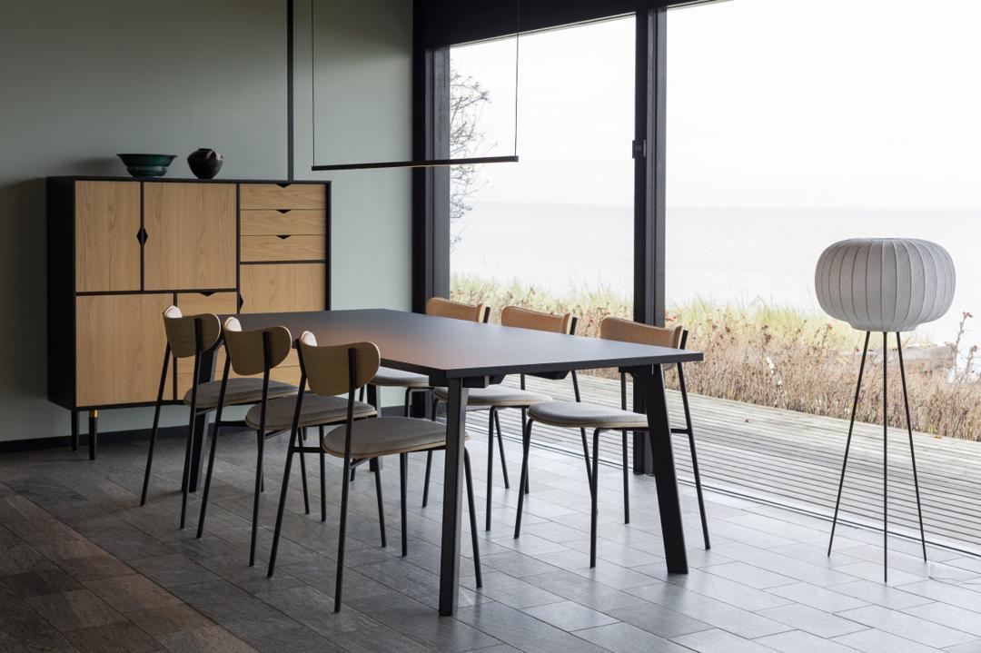 Moderne spisestue med sort spisebord, træstole, skænk i egetræ og store vinduer med udsigt i stilren skandinavisk indretning.