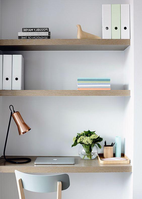 Minimalistisk skriveplads med væghylder, bøger, lampe, plante og bærbar på enkelt træbord.