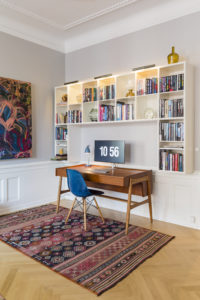 Hjemmekontor med bogreol, træfarvet skrivebord, blå stol og rødt gulvtæppe.