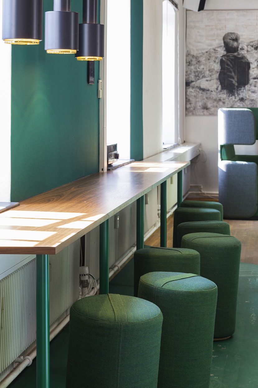 Fællesområde på arbejdsplads med grønne stole og et langt bord.